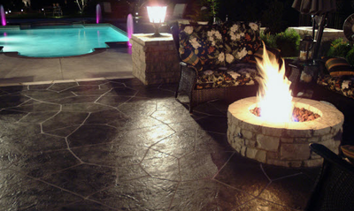 Stamped concrete fire pit along side of a concrete pool deck and a lighted outdoor light.
