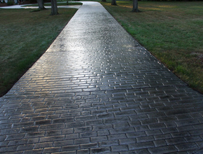 Long driveway with a gray brick stamped design performed by Lansing stamped concrete.